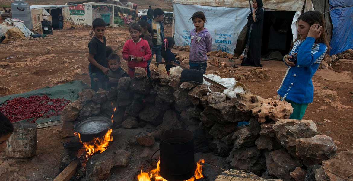 Kinder stehen in einem Camp um die Kochstelle im Freien herum: Der nahende Winter bedroht die vielen obdachlos gewordenen Familien im Nahen Osten.