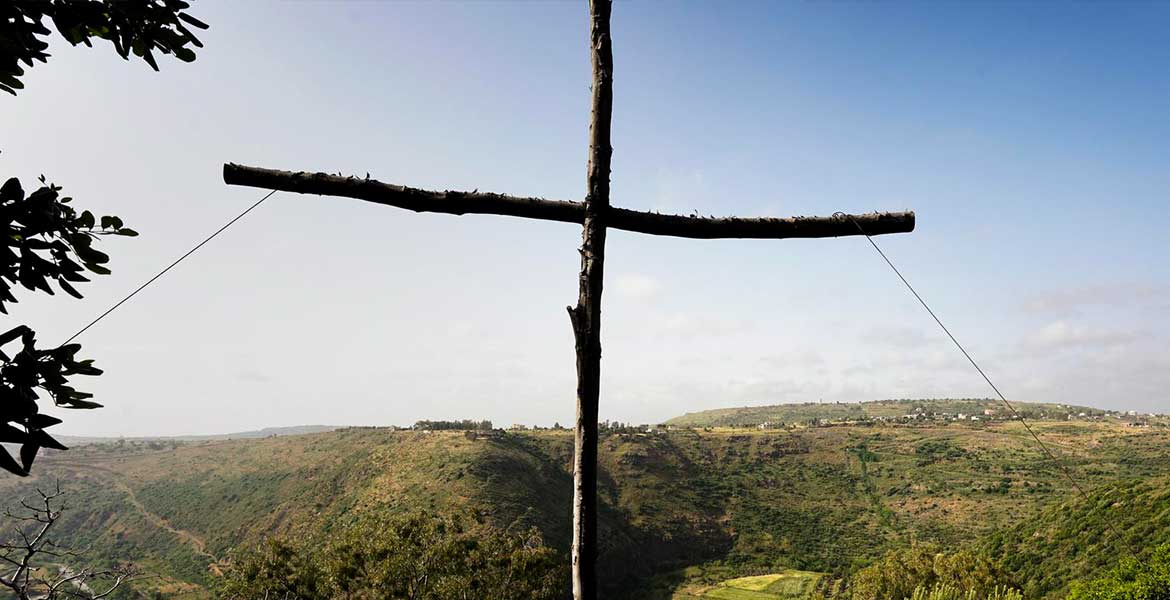 Blick in den Norden Syriens. Im Vordergrund ein einfaches Holzkreuz aus dünnen, wenig bearbeiteten Baumstämmen.