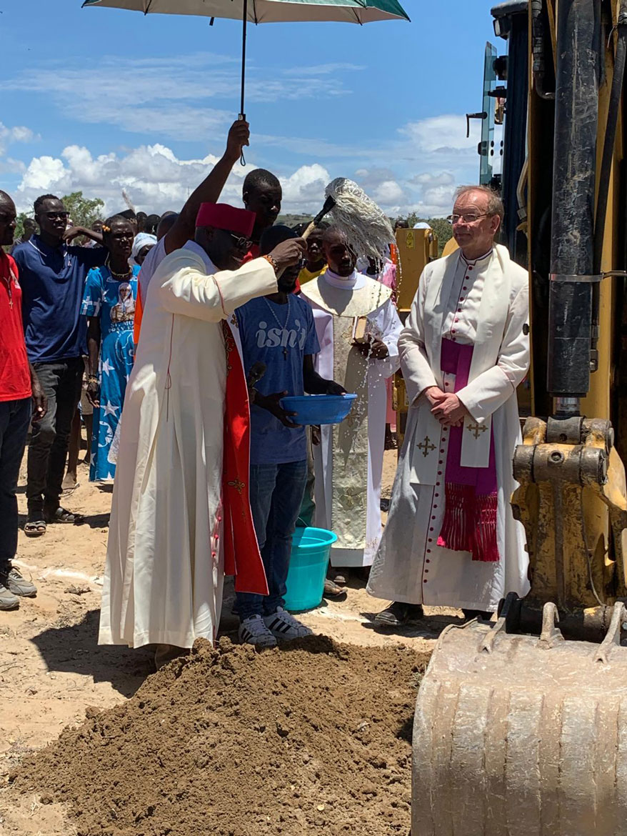 Der örtliche Bischof weiht den Bagger, der auf der Baustelle zum Einsatz kommen soll, mit reichlich Weihwasser.