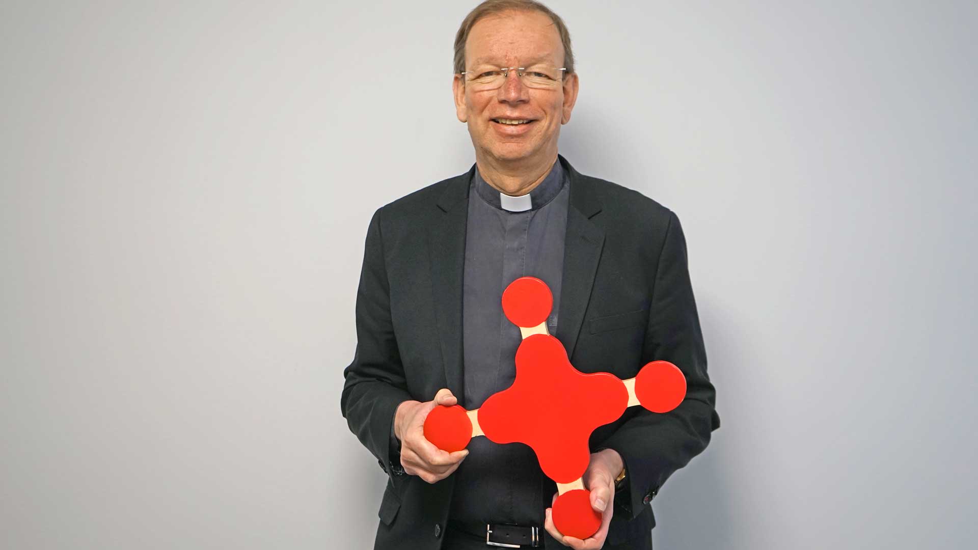 missio-Präsident Monsignore Wolfgang Huber hält das missio-Kreuz aus Holz vor sich.