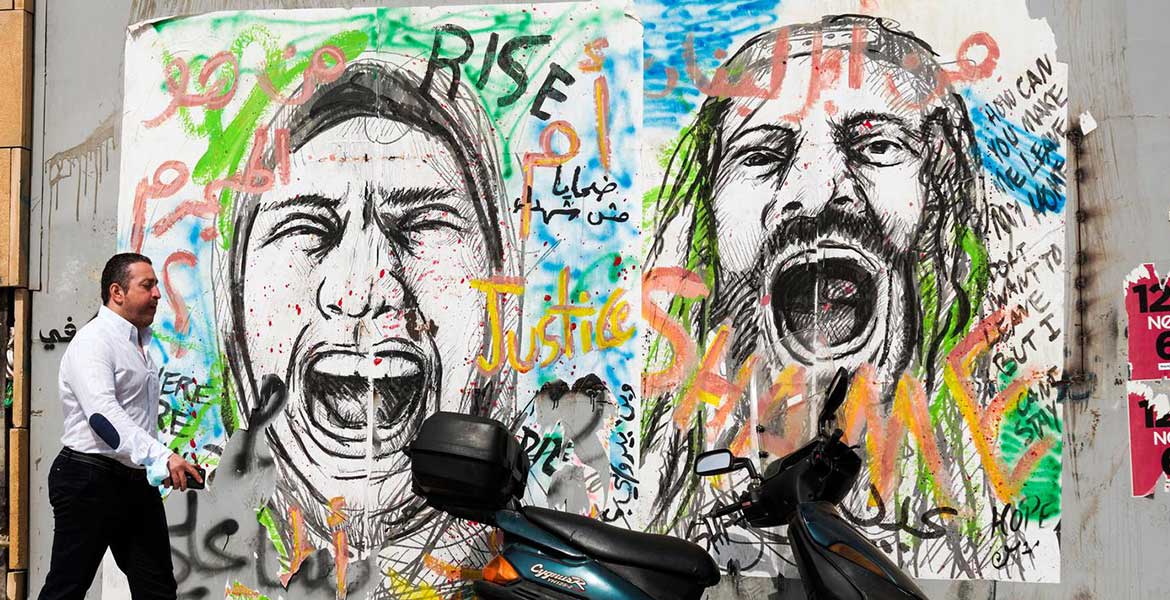 Ein Mann geht an einem großformatigem Grafitti vorbei, das in schwarz-weiß und stark vergrößert die schreienden Gesichter einer Frau mit Kopftuch und eines bärtigen Mannes zeigt. Um die Gesichter herum sind grüne und blaue Farbflächen sowie verschieden große Schriftzüge auf Englisch und Arabisch zu sehen mit Inhalten wie Scham oder Gerechtigkeit.