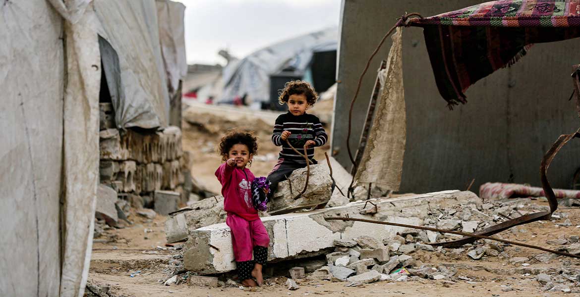 Zwei Kinder sitzen in einem Flüchtlingslager in Gaza auf den Trümmern eines Hauses.