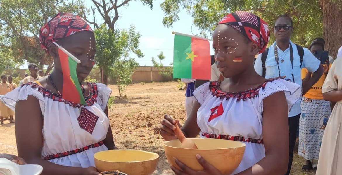 Zwei junge Frauen aus Burkina Faso haben zwei Holzschüsseln in der Hand und sind geschmückt mit burkinischen und deutschen Flaggen.