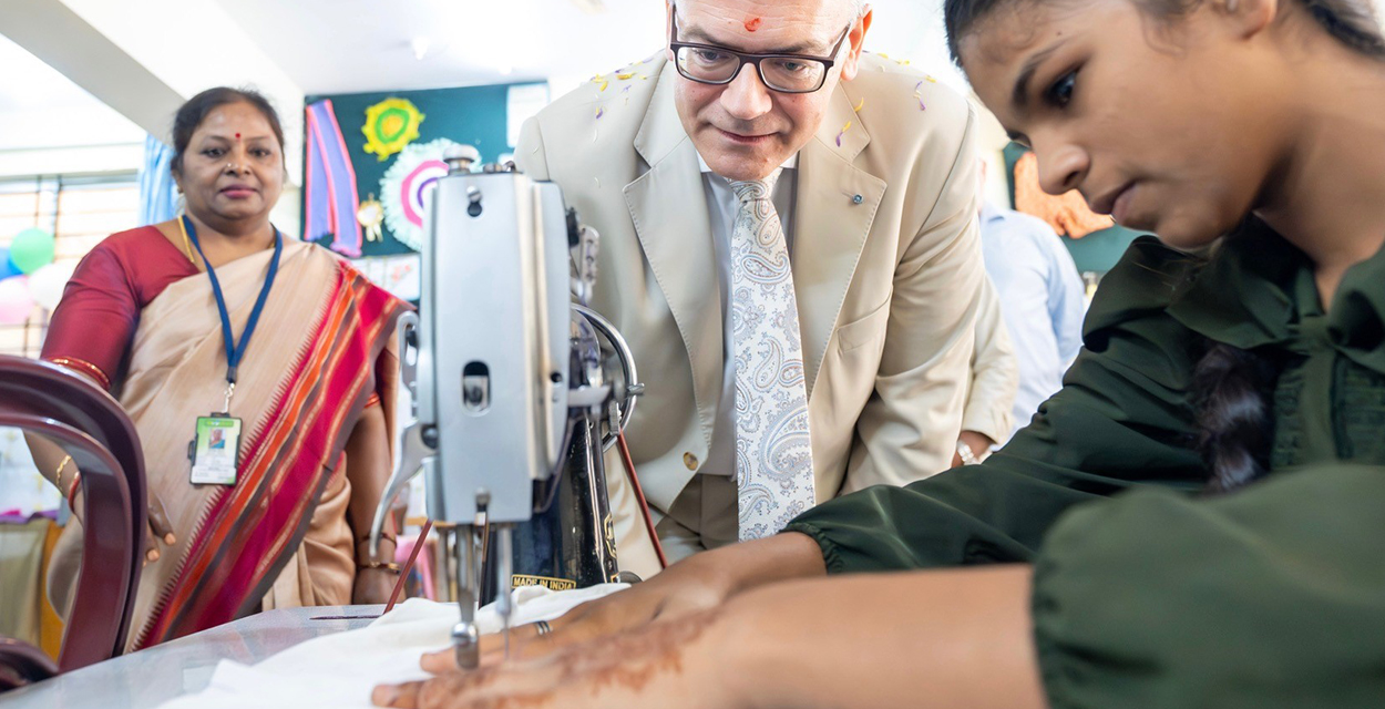 Staatsminister Dr. Florian Herrmann sieht sich in einer Werkstatt des missio Projektpartners BREADS an, wie eine junge Inderin mit der Nähmaschine arbeitet. Foto: Bayerische Staatskanzlei