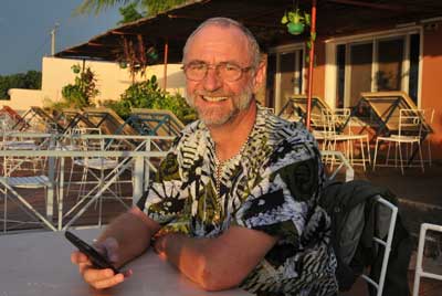 Der in Mali entführte Afrikamissionar Hajo Lohre sitzt an einem Tisch und hat sein Handy in der Hand. Die Sonne steht tief und scheint ihm ins Gesicht. Er blickt den Betrachter an und lächelt. Foto: Raphael Athens