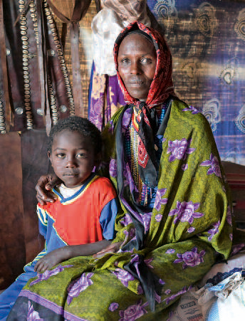 Eine Äthiopierin mit buntem Umhang und gemustertem Koptuch sitzt in einer Hütte. Neben ihr ein Junge im Grundschulalter, um den sie den Arm legt. Beide blicken in die Kamera.