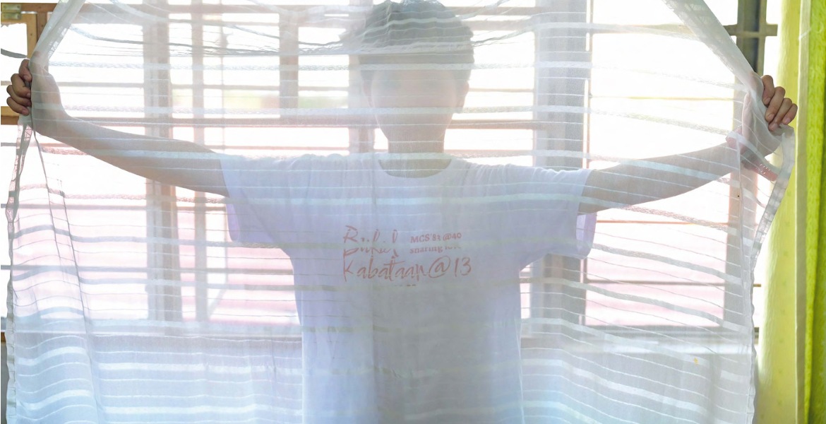 Ein Kind, das im Schutzhaus untergekommen ist, steht hinter einem halbtransparenten Vorhang, den es mit beiden Händen hält.