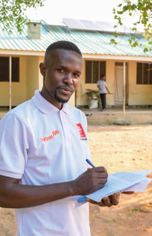 Barnabas Oloya blickt von seinen Unterlagen auf. Er steht auf einem Platz vor einem Gebäude.