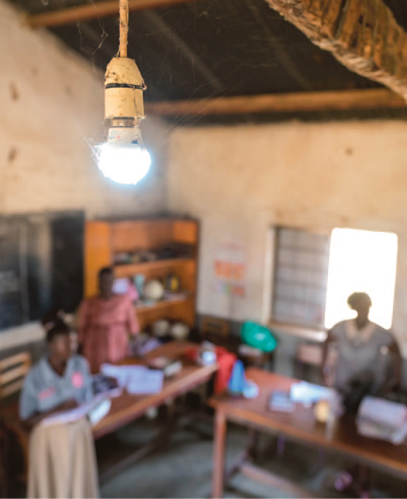 Eine nackte Glühbirne in einer alten Fassung voller Spinnweben leuchtet an der Decke. Verschwommen sieht man in leichter Draufsicht drei Personen in einem spärlich ausgestatteten Raum.