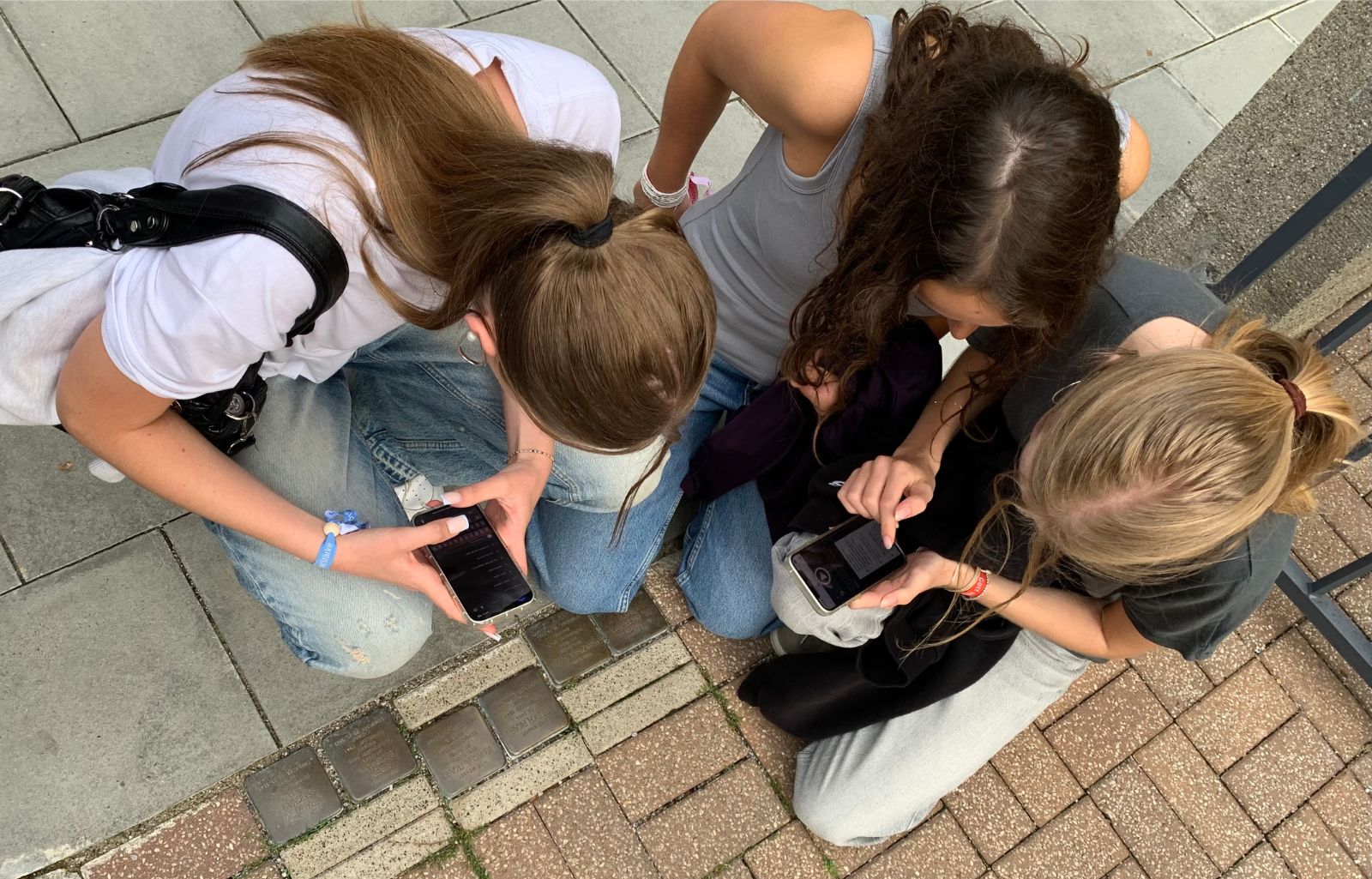 Drei Teilnehmerinnen des Mitmachtags beugen sich über die Stolperstein in der Heinrich-Heine-Straße 5 und beantworten die entsprechende Quizfrage in der Actionbound-App.
