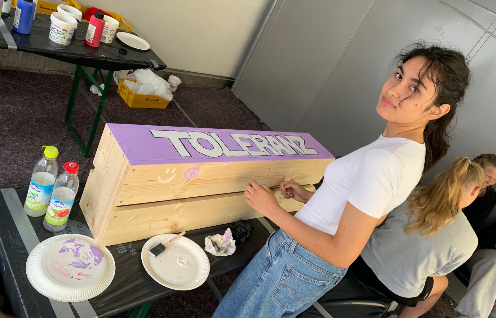 Eine Teilnehmerin des Mitmachtags steht im Kreativbereich vor ihrem Holzbaustein mit dem Schriftzug "Toleranz".