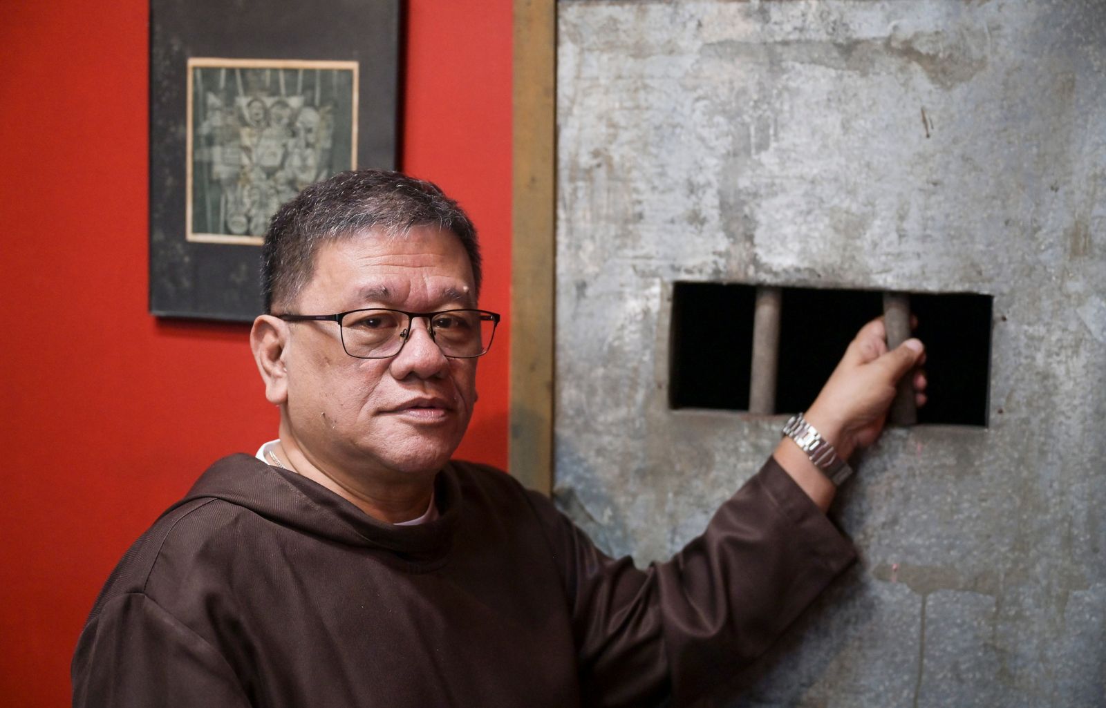 Father Toots hält sich mit der linken Hand am Gitterstab einer nachgevbildeten Gefägniszelle fest und guckt den Betrachter gedankenverloren an.