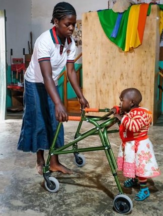 Eine junge Frau hält einem Kleinkind einen Gehwagen hin