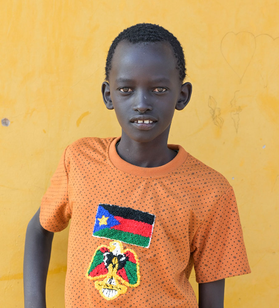 Ein Junge blickt in die Kamera. Er trägt ein T-Shirt mit südsudanesischer Flagge.