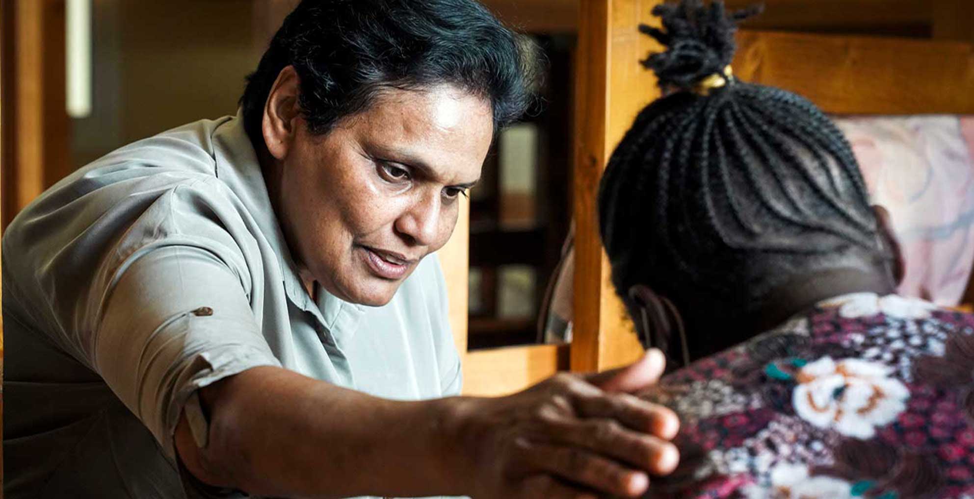 Die Mitarbeiterin eines Schutzhauses legt einer anderen Frau, die nur von hinten zu sehen ist, eine Hand auf die Schulter, um sie zu trösten.