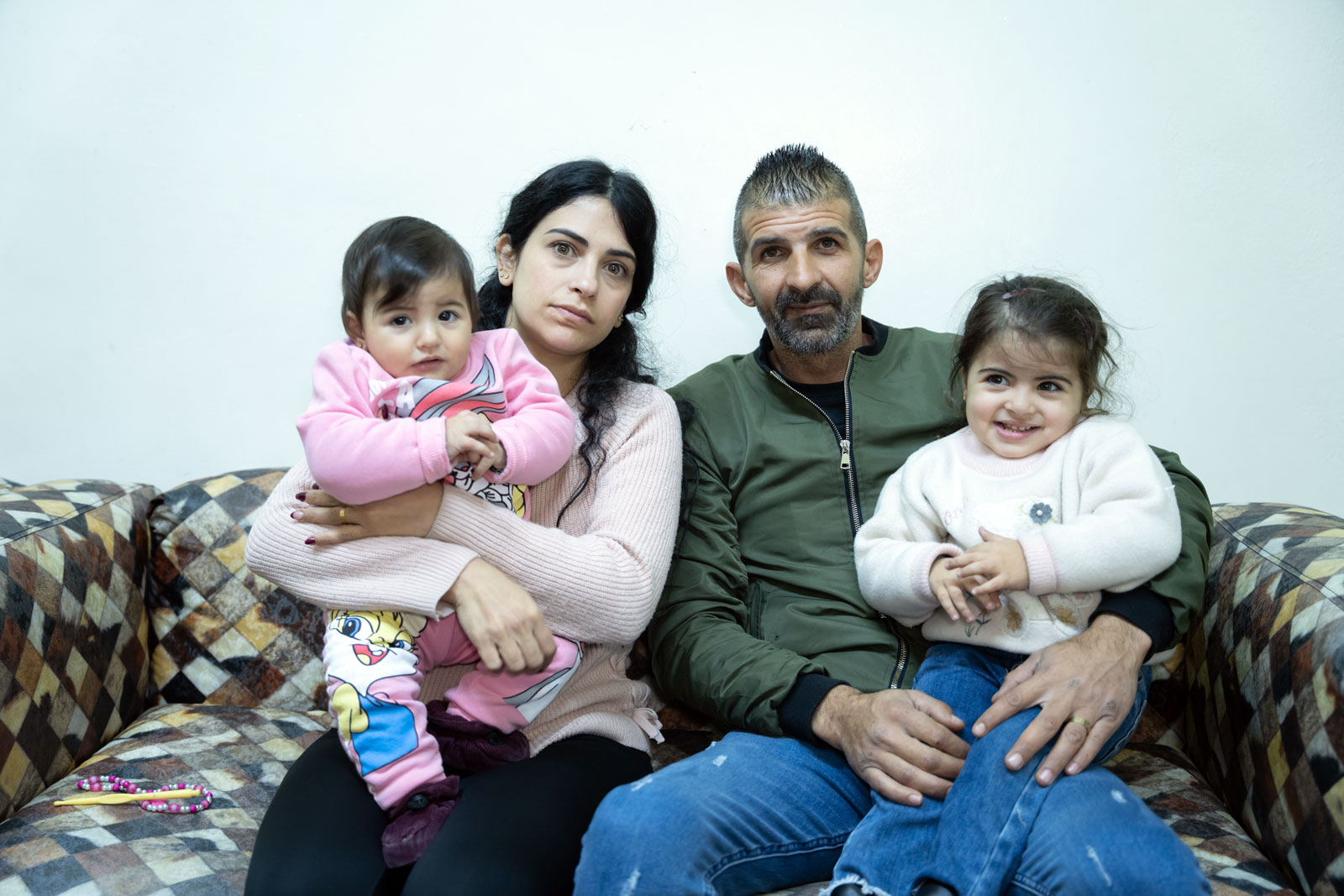 Eine geflüchtete Familie - Eltern und zwei junge Mädchen - sitzen in Beirut auf einem Sofa