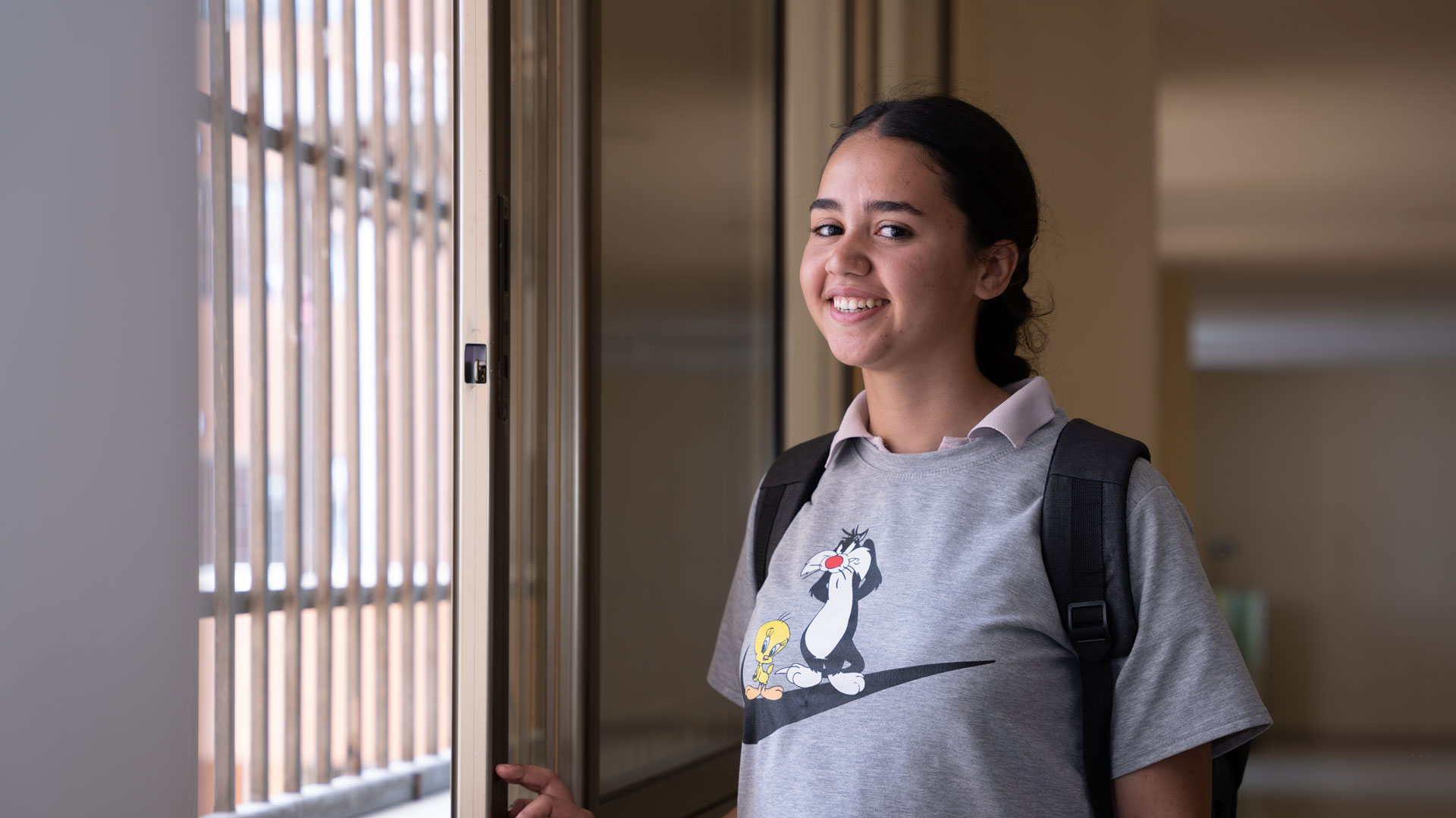 Das Mädchen Sophie steht in einem Gang und lächelt - sie freut sich, dass sie zur Schule gehen und lernen darf.