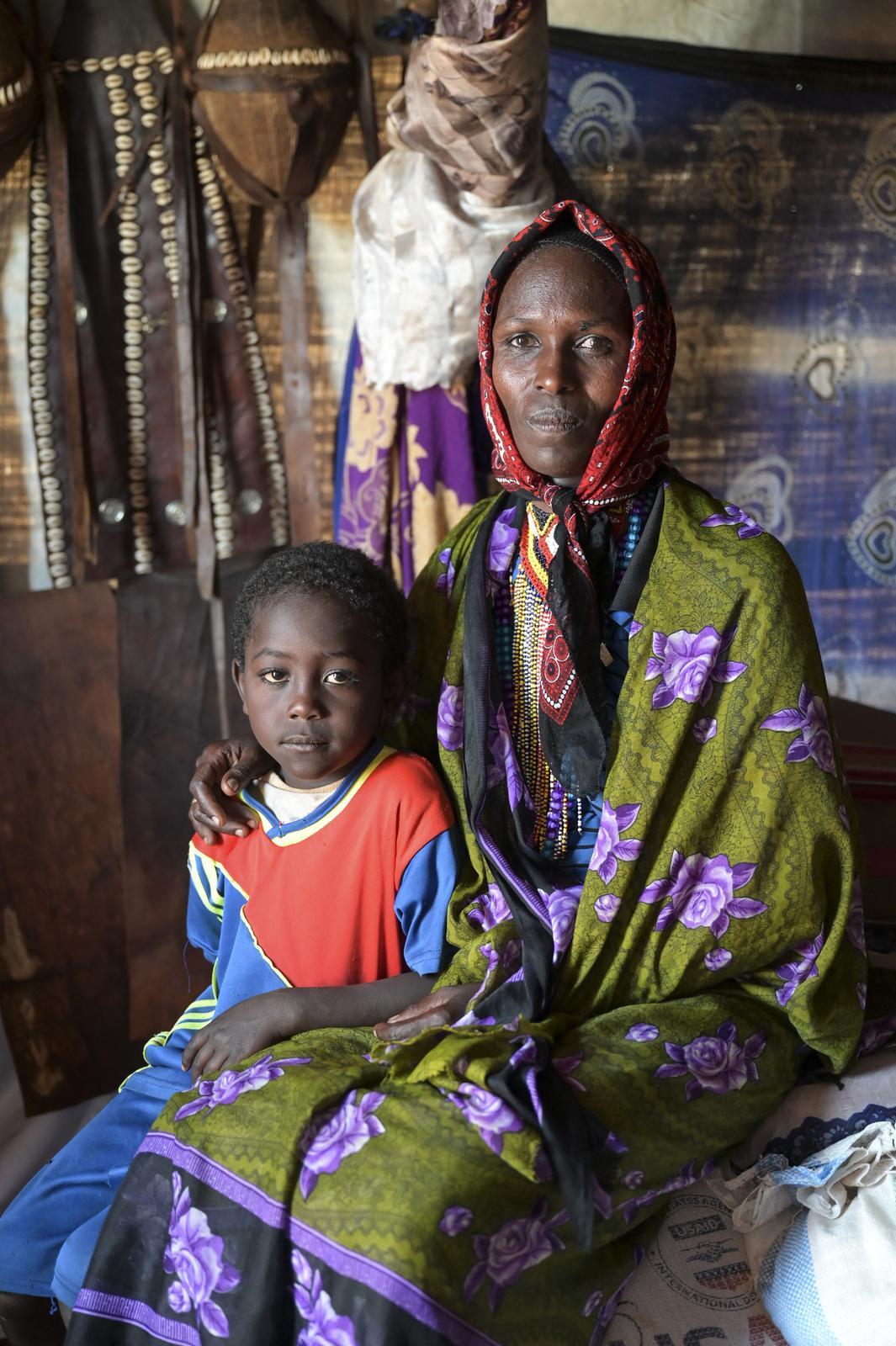 Eine Frau aus Südäthiopien sitzt mit ihrem Kind auf dem Schoß in ihrem provisorischen Zelt. Beide blicken ernst in die Kamera. 