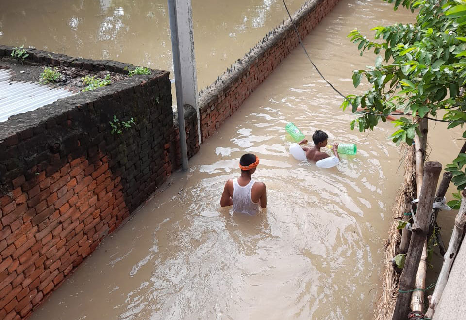 Ein Mann watet mit einem Jungen, bepackt mit leeren Trinkbehältern, durch eine überflutete Straße