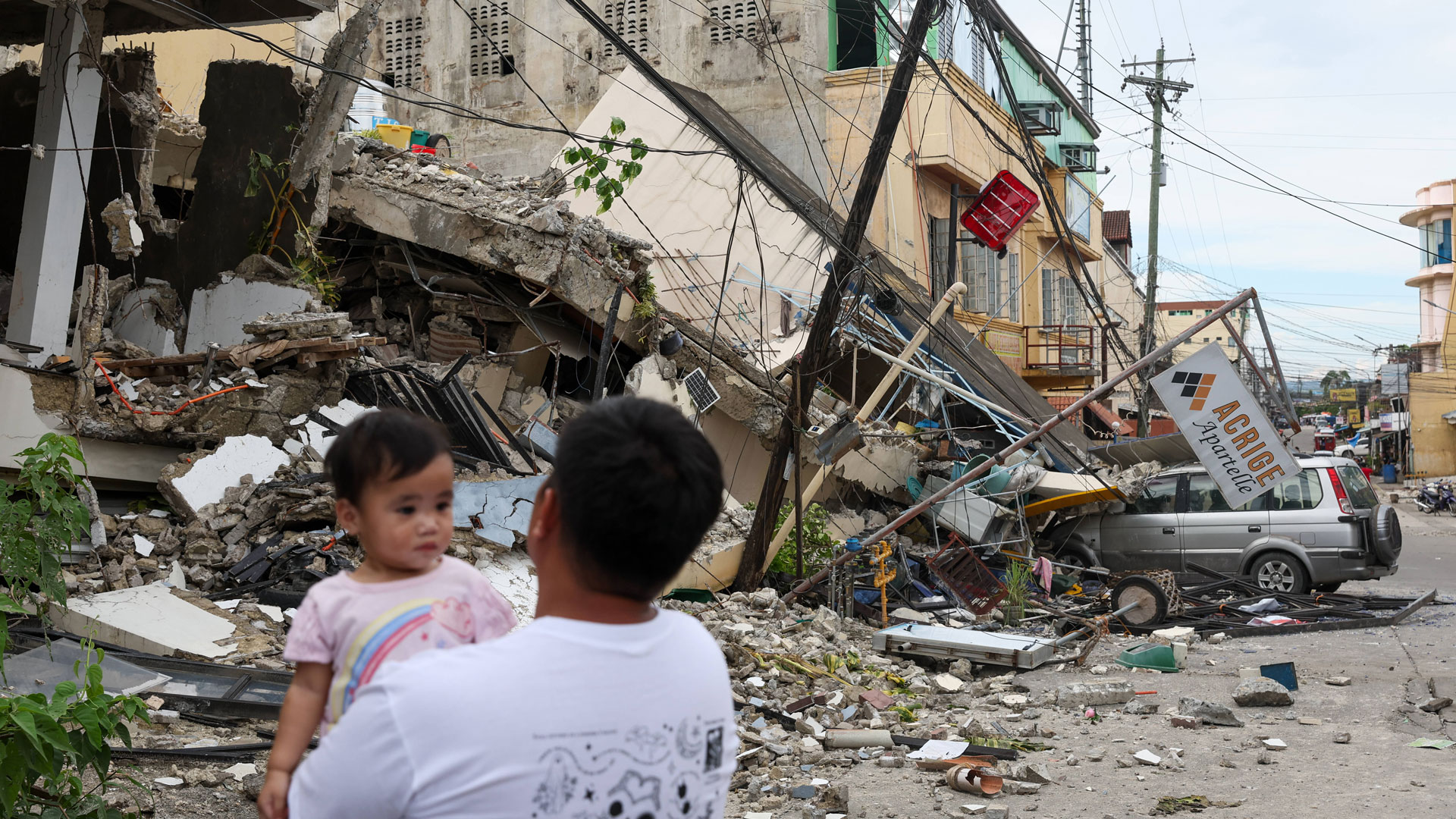 Ein Mann mit einem Kind auf dem Arm steht vor einem vom Erdbeben völlig zerstörten Gebäude in Bogo City in der Region Cebu auf den Philippinen