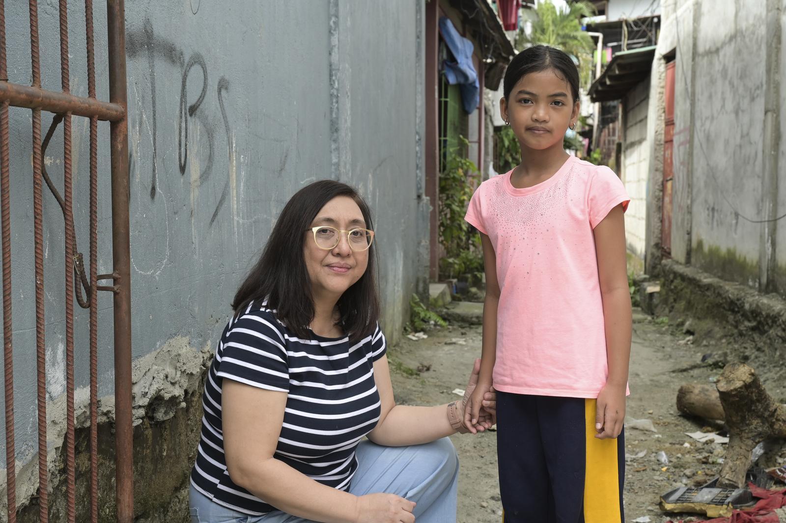 Projektpartnerin Carol Daria kniet neben Yessa, einer Halbwaise, in einer Gasse in Payatas im Großraum Manila