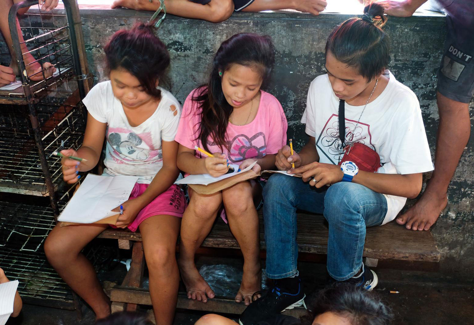 Kinder schreiben in Schulhefte, die sie auf den Knien halten.