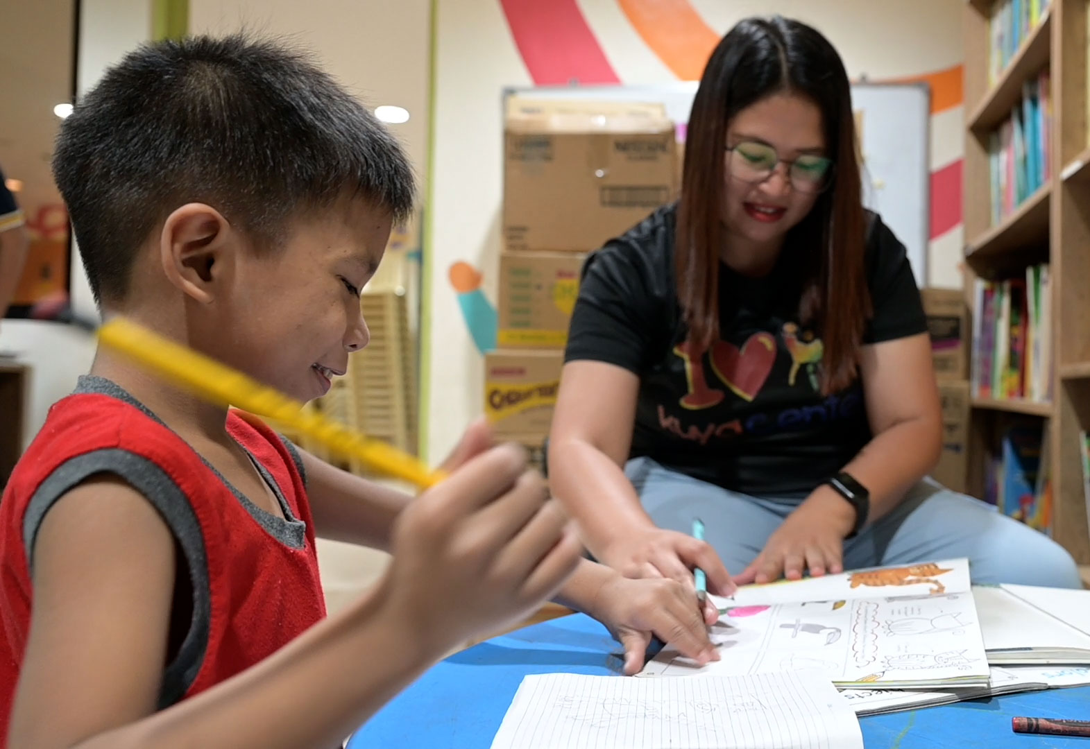 Ein Junge und eine Betreuerin sitzen über Schulheften.