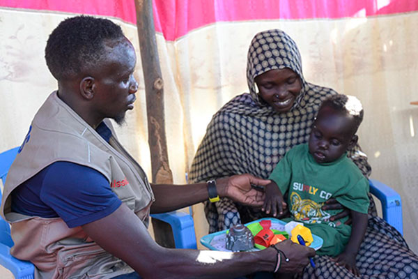 Ein Helfer kümmert sich um eine Mutter mit Kind in einem Flüchtlingscamp