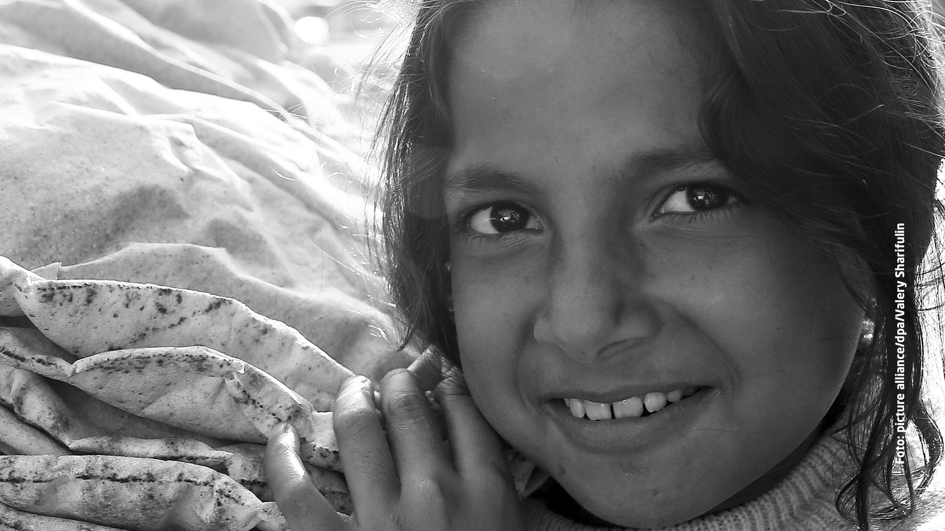 Nahrungsmittelhilfe für Familien in Syrien: Ein Mädchen trägt Fladenbrot und lächelt