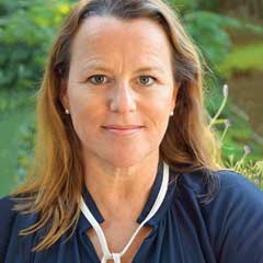 Porträt von Sabine Brink. Sie trägt die mittelbraun gefärbten, langen Haare offen und hat eine dunkelblaue Bluse an.