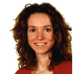 Porträt Deborah Wiegert. Die junge Frau hat eine rote Bluse an und trägt das dunkle, wellige Haar offen und lächelt in die Kamera.