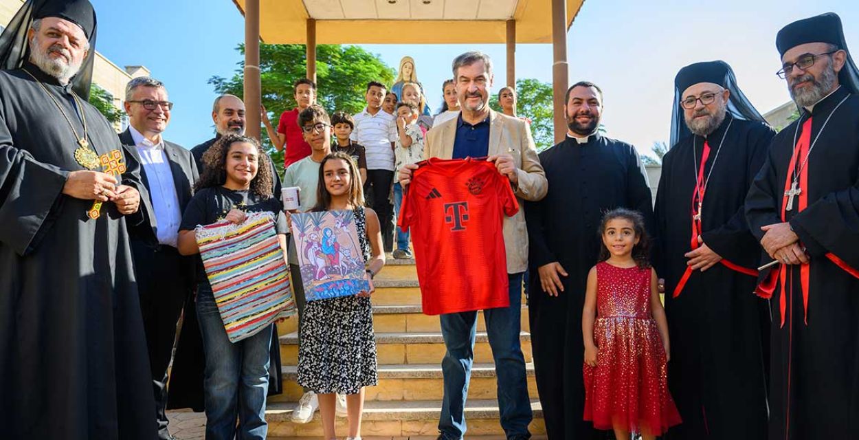 Bayerns Ministerpräsident Söder und Mitglieder der Bayerischen Staatskanzlei zu Besuch in einem missio-Projekt in der koptisch-katholischen Diözese Gizeh in Ägypten. Söder hält ein rotes Telekom-T-Shirt vor sich. Neben ihm Priester, aber auch Kinder, die zum Teil ebenfalls Gastgeschenke zeigen. Foto: Bayerische Staatskanzlei