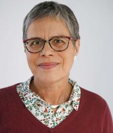 Porträt von Carola Meier. Sie blickt freundlich und zurückhaltend in die Kamera. Ihr graues Haar ist kurz geschnitten. Sie trägt eine gemusterte Brille, die farblich gut zu ihrer Bluse und dem bordeauxroten Pullover darüber passt. 
