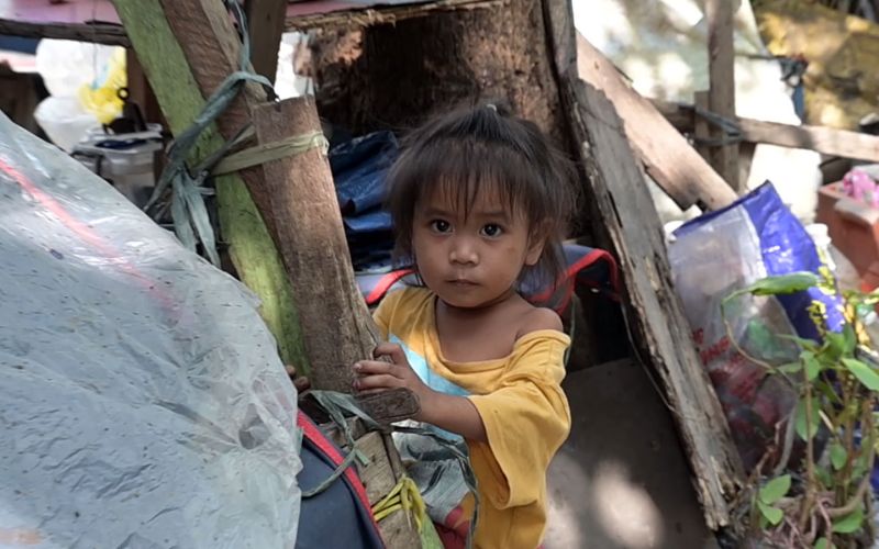 Ein philippinisches Kind blickt vorsichtig aus einem Holzverschlag