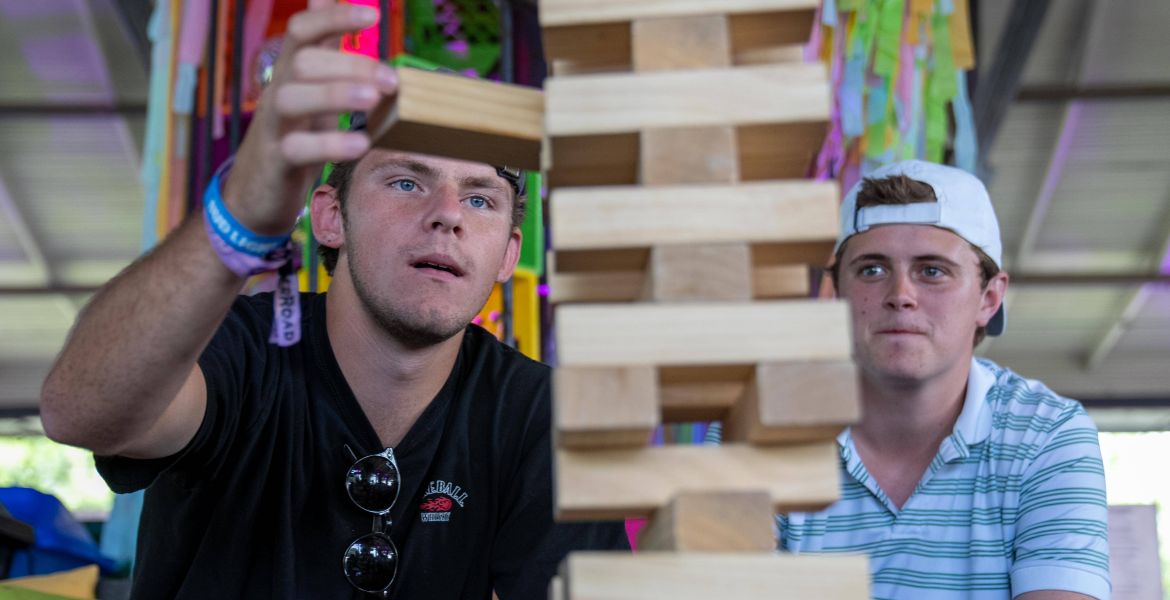 Zwei junge Männer bauen einen Holzturm aus Jenga-Steinen.