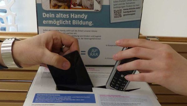 Zwei Hände in Großaufnahme werfen jeweils ein Handy in den Schlitz einer missio-Handyaktionsbox.