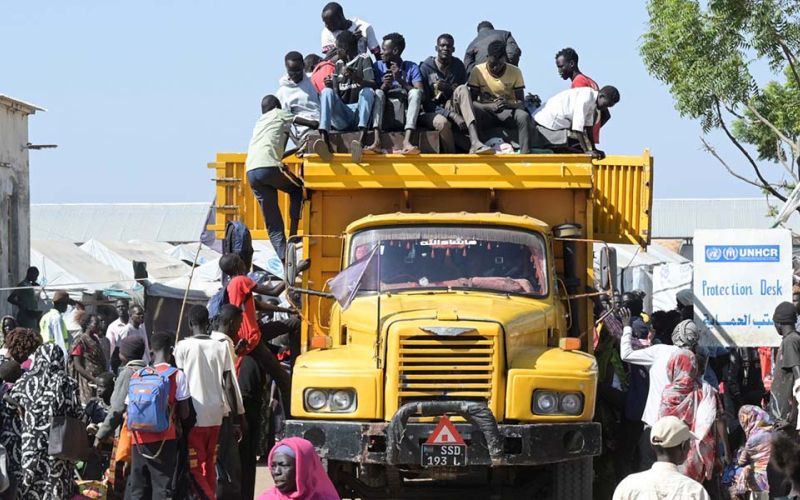 Geflüchtete in einem Flüchtlingslager in Renk im Südsudan. Sie sitzen teis auf einem riesigen gelben LKW, andere bewegen sich um das Fahrzeug herum.
