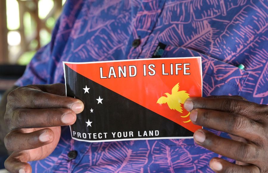 Eine indigene Frau hält die Flagge von Papua-Neuguinea in die Kamera. Zu sehen sind nur die Flagge und die Hände der Frau.