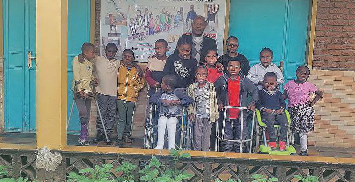 Gruppenfoto von Kindern mit Behinderung mit Rollstühlen, Krücken und Gehvorrichtungen gemeinsam mit Pater Mathewos auf einer Veranda des Reha-Zentrums in Äthiopien.. 