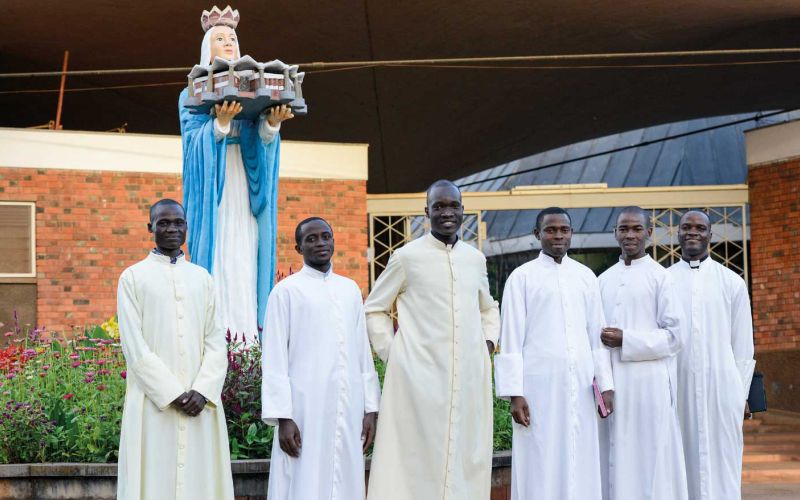 Gruppenfoto von sechs Priesteramtskandidaten in Uganda, alle in weiß gekleidet.