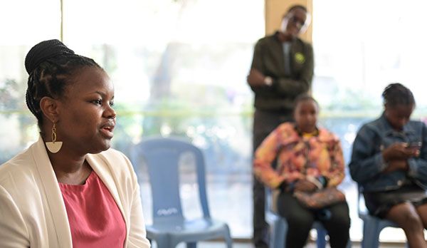 In einem Raum sitzt im Vordergrund missio-Projektpartnerin Winnie Mutevu bei einem Workshop und spricht in die Runde. Im Hintergrund verschwommen sieht man zwei sitzende Frauen und einen stehenden Mann.