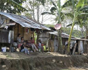 Menschen sitzen auf der philippinischen Insel Mindanao vor ihren ärmlichen mit Wellblech bedeckten Behausungen. Dazwischen wachsen Palmen.