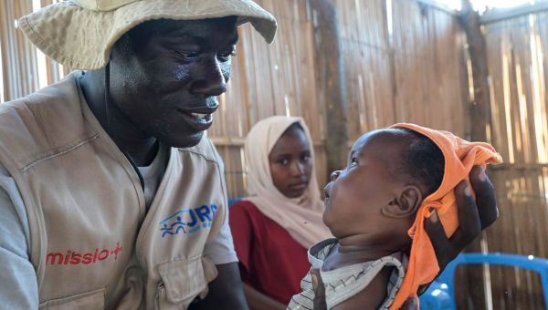 Ein Mitarbeiter des Jesuiten Flüchtlingsdienstes hält das Baby einer geflüchteten Frau im Arm. Er betreut Geflüchtete aus dem Sudan in einem Camp im Südsudan.