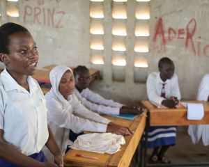 Schülerinnen an der Blue State Secondary des JRS in Kenia sitzen in einem Klassenzimmer. Ein Mädchen im Vordergrund steht und spricht in Richtung Tafel nach vorne.