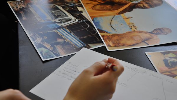 Auf einem Tisch liegen drei große Fotos mit Motiven aus Afrika. Im Vordergrund