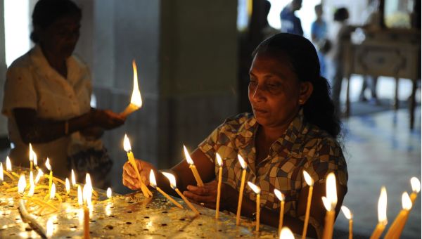 Eine Frau zündet in einer dunklen Kirche Kerzen an.