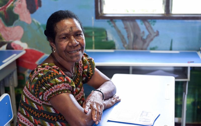 Eine erwachsene Frau sitzt in einer Schulbank in Papua-Neuguinea und lächelt in die Kamera.
