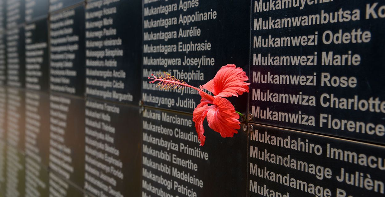 Gedenktafel aus schwarzem Stein mit den Namen der Opfer des Genozids in Ruanda im Jahr 1994. Darauf steckt eine rote Hibiskusblüte.