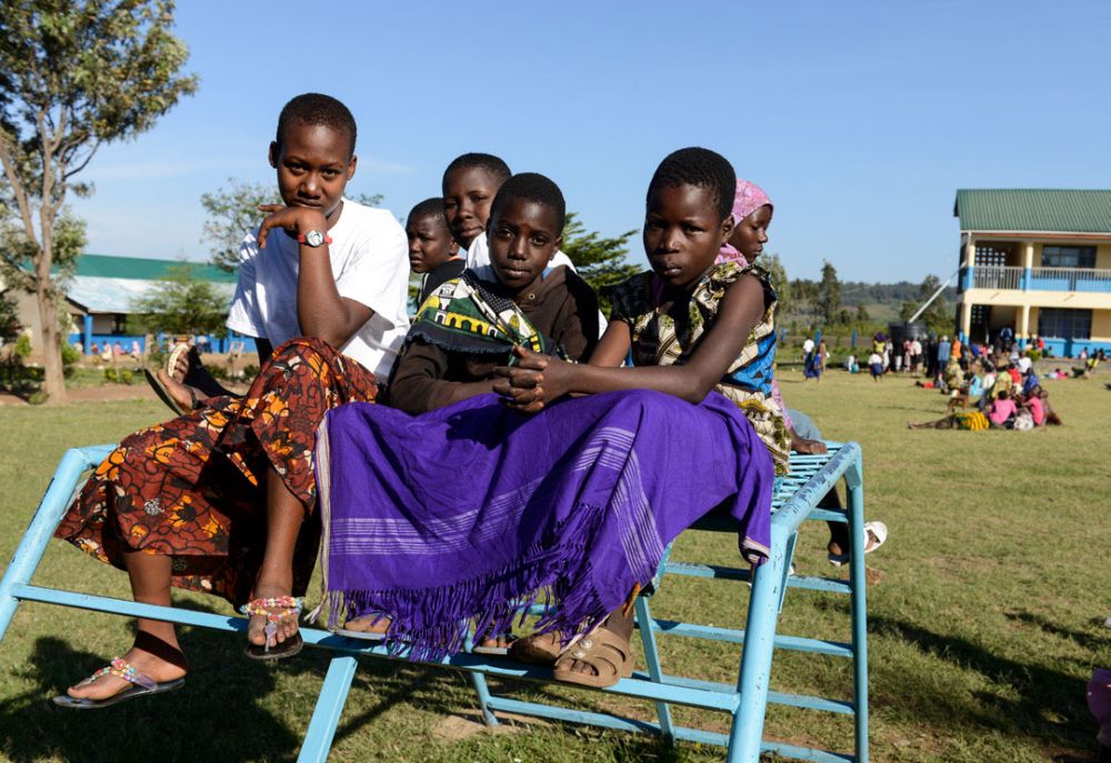 Vier Mädchen sitzen auf einem Klettergerüst in einem großen begrünten Hof und schauen ernst in die Kamera.