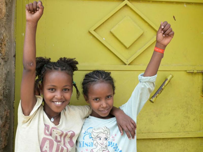Zwei Mädchen aus dem Waisenhaus St. Clare recken die Arme hoch in die Luft.